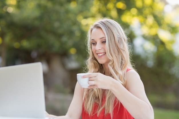 Frau, die Kaffee beim Verwenden des Laptops hat