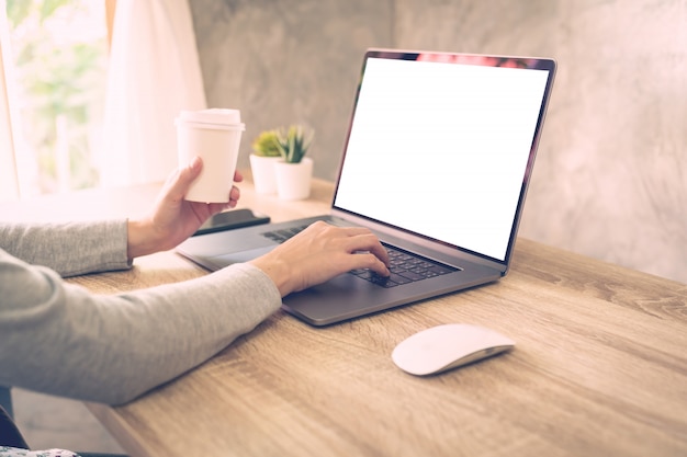 Frau, die Kaffee hält und Laptop auf Holztisch im Büro verwendet