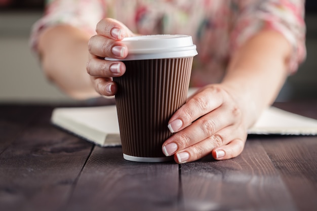 Frau, die Kaffee zum Mitnehmen am Tisch hält