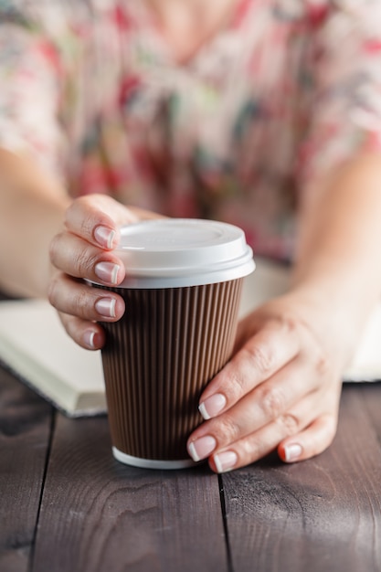 Frau, die Kaffee zum Mitnehmen am Tisch hält