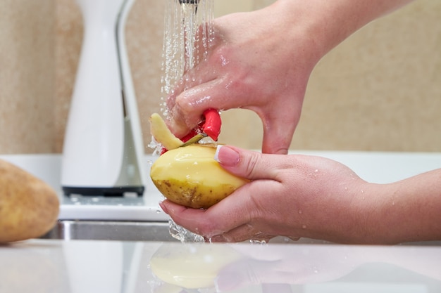 Frau, die Kartoffeln über einem Waschbecken schält, Nahaufnahme