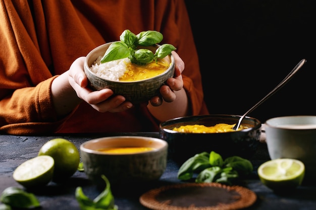 Frau, die Keramikschale des gelben Curry hält, serviert mit Basilikum und Limetten