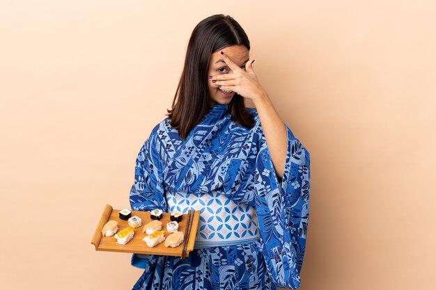Frau, die Kimono trägt und Sushi über Wand hält, das Augen durch Hände bedeckt und lächelt