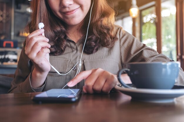 Frau, die Kopfhörer hält, während Musik mit Handy im Café hört