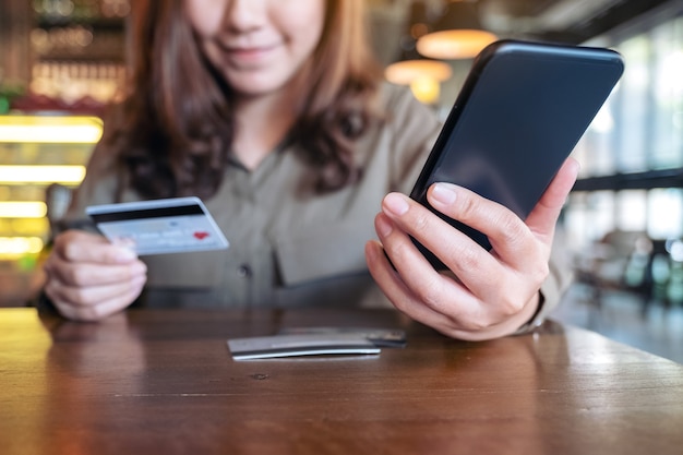 Frau, die Kreditkarte hält und Mobile Banking beim Sitzen im Café verwendet