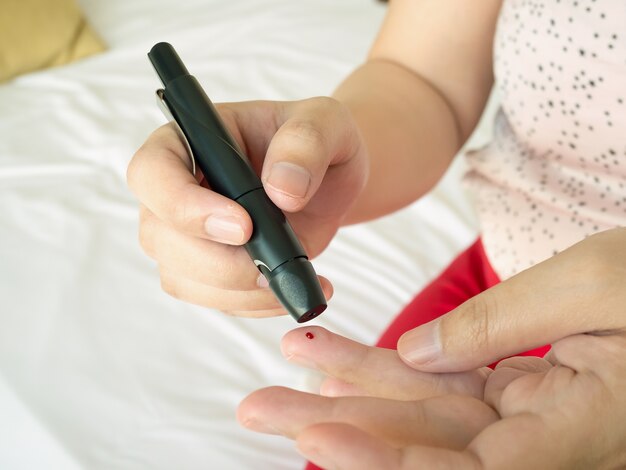 Frau, die Lanzette am Finger verwendet, Diabetes-Test, der Blutzuckerspiegel prüft