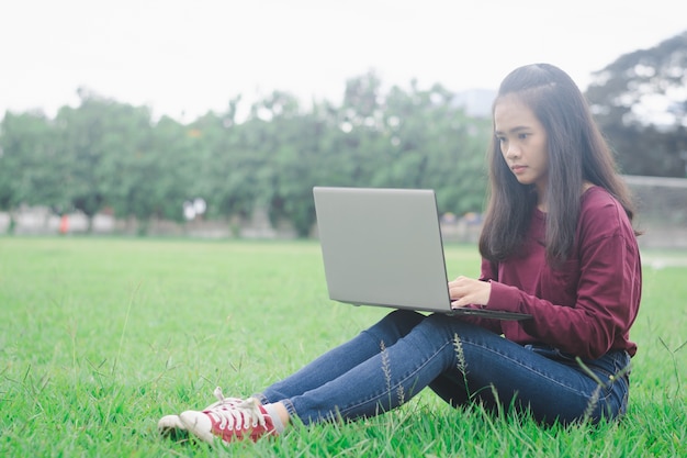 Frau, die Laptop auf grünem Feldhintergrund verwendet