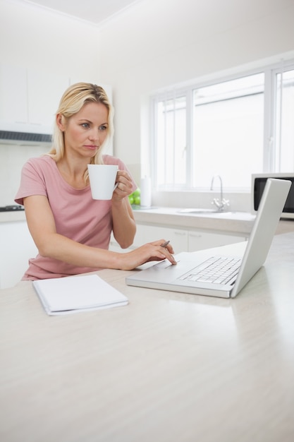 Frau, die Laptop beim Trinken des Kaffees in der Küche verwendet