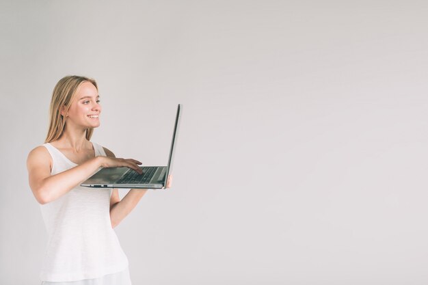 Frau, die Laptop-Computer lokalisiert auf grau hält. Mädchen im weißen Hemd.