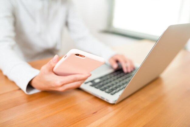 Frau, die Laptop mit Mobiltelefon verwendet