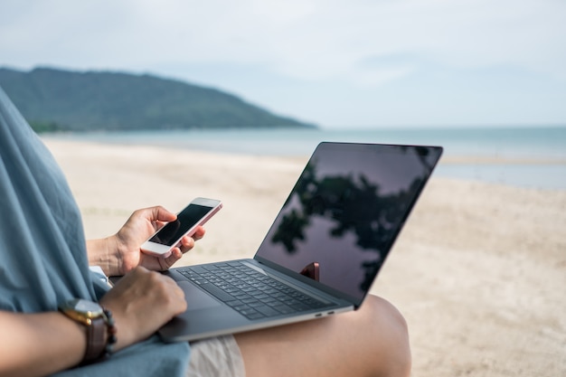 Frau, die Laptop und Smartphone verwendet, um Studie im Urlaub Cady am Strand Hintergrund zu arbeiten.