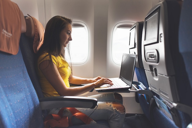 Frau, die Laptop verwendet, während im Flugzeug nahe Fenster sitzt.