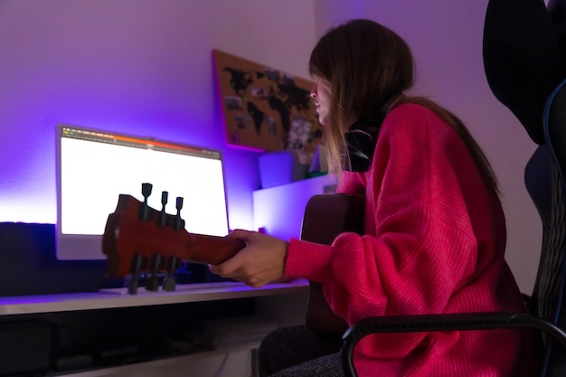 Frau, die lernt, Gitarre zu spielen, mit Online-Kursen auf dem Computer