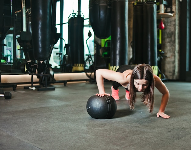 Frau, die Liegestütze mit Medizinball im dunklen Fitnessstudio tut