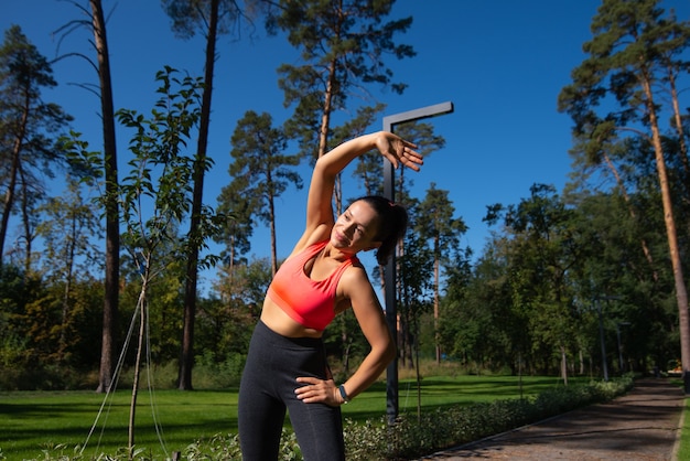 Frau, die linke Seite des Körpers streckt, nachdem sie im schönen grünen Park trainiert