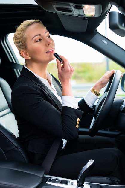 Frau, die Lippenstift beim Fahren ihres Autos verwendet