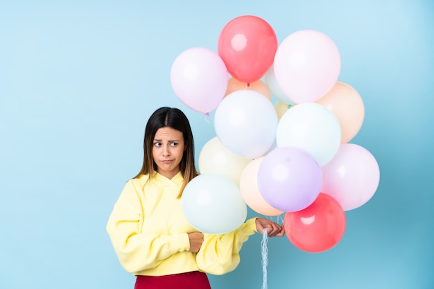 Frau, die Luftballons in einer Partei über isolierter blauer Wand hält, die eine Idee denkt