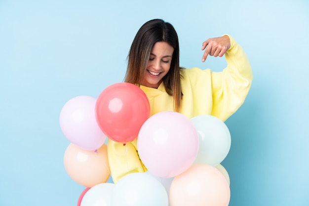 Frau, die Luftballons in einer Partei über isolierter blauer Wand hält