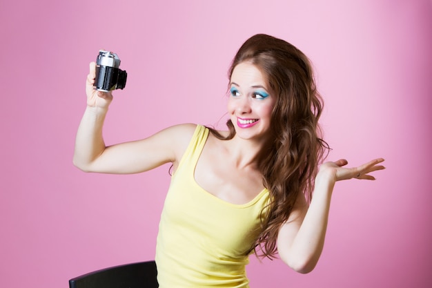 Frau, die Make-up mit einer Kamera auf rosa Hintergrund trägt