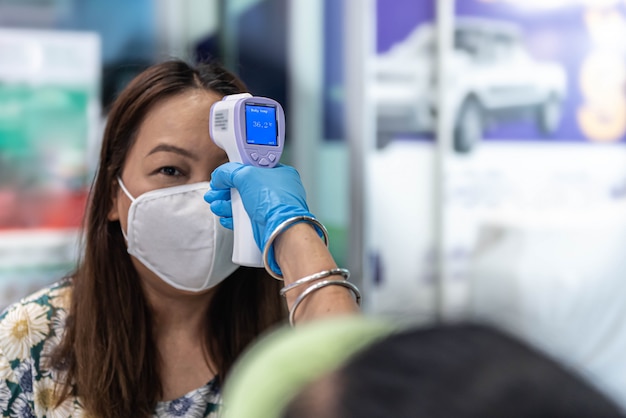 Foto frau, die maske mit thermoscan- oder thermometerpistolen trägt, die auf coronavirus prüfen