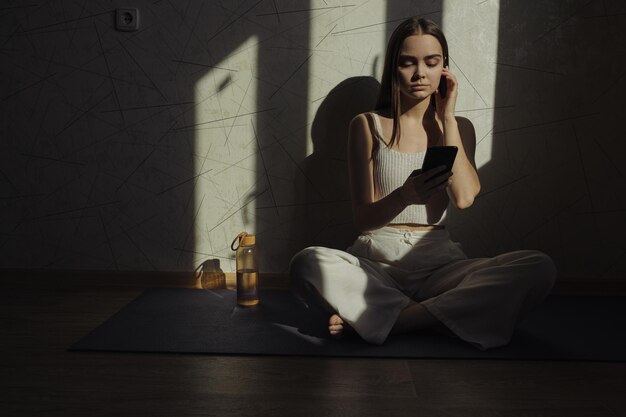 Frau, die Meditationsmusik in Ohrstöpseln über Smartphone hört, während sie in Lotus-Pose sitzt