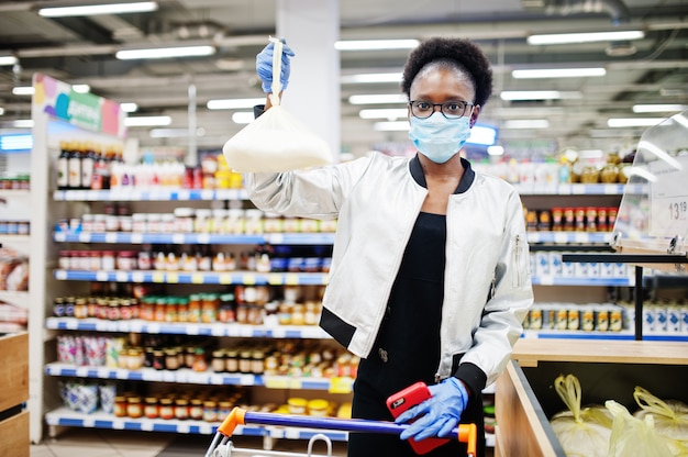 Frau, die medizinische Einwegmaske und Handschuhe trägt, die im Supermarkt während des Ausbruchs der Coronavirus-Pandämie einkaufen.