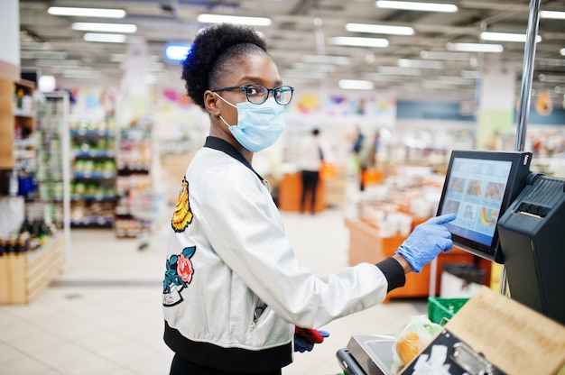 Frau, die medizinische Einwegmaske und Handschuhe trägt, die im Supermarkt während des Ausbruchs der Coronavirus-Pandämie einkaufen.