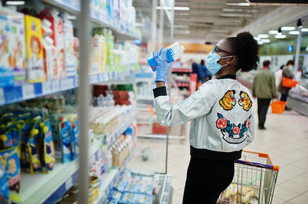 Frau, die medizinische Einwegmaske und Handschuhe trägt, die im Supermarkt während des Ausbruchs der Coronavirus-Pandämie einkaufen.