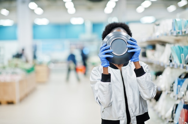 Frau, die medizinische Einwegmaske und Handschuhe trägt, die im Supermarkt während des Ausbruchs der Coronavirus-Pandämie einkaufen.