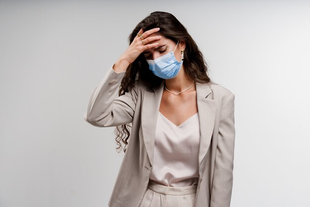Frau, die medizinische Maske trägt, lokalisiert auf weißem Hintergrund, der Kopfschmerz hat