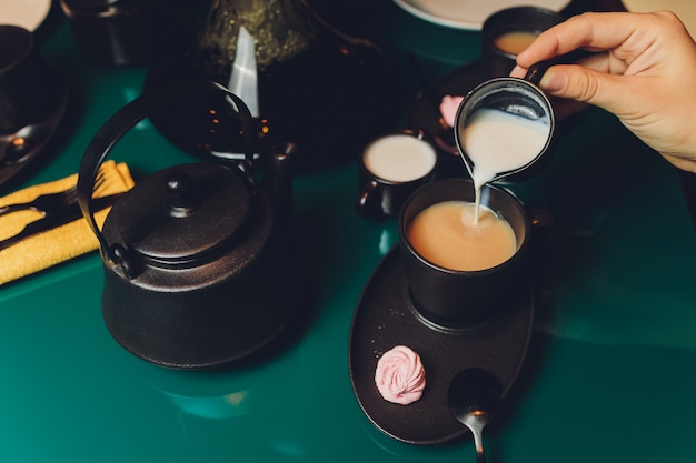 Frau, die Milch in der Tasse Tee vom Kessel gießt.