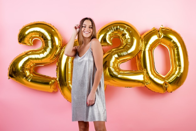 Frau, die mit 2020 Ballonen des neuen Jahres tragen das Kleid lokalisiert über Rosa lächelt