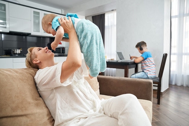 Frau, die mit Baby spielt, während Teenager auf Laptop studiert