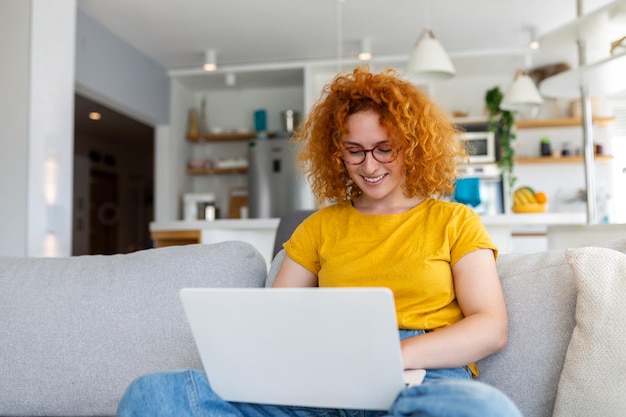 Frau, die mit Computer auf Sofa sitzt und zu Hause E-Learning und freiberufliches Jobkonzept lernt