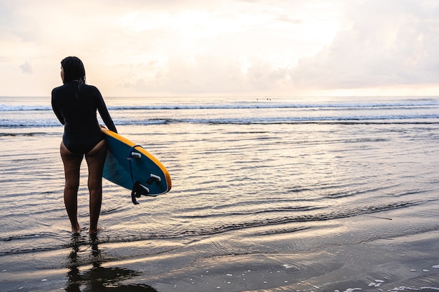 Frau, die mit einem Surfbrett am Strand steht