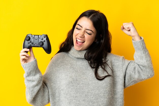 Frau, die mit einem Videospiel-Controller spielt, der auf gelber Wand einen Sieg feiert