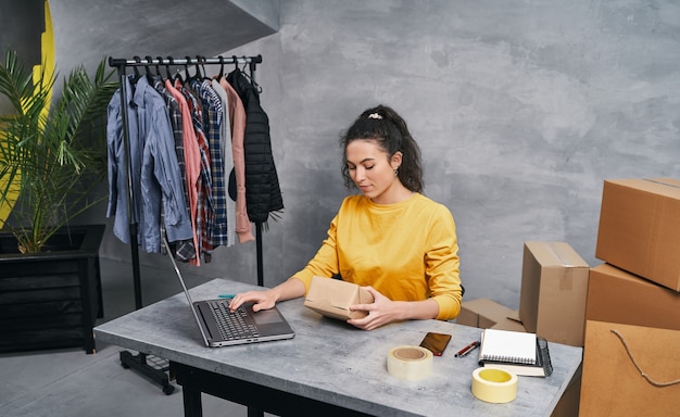 Frau, die mit ihrem Laptop von zu Hause aus ein Paket sendet