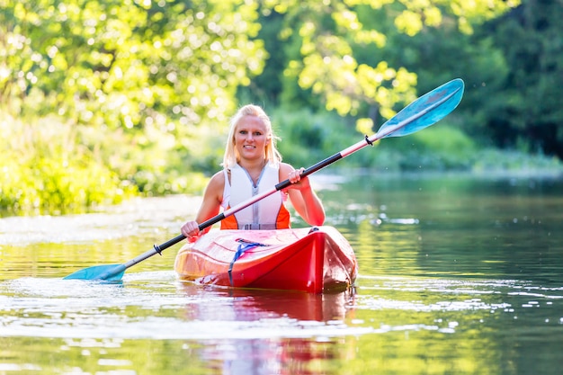 Frau, die mit Kajak auf Waldfluß fährt