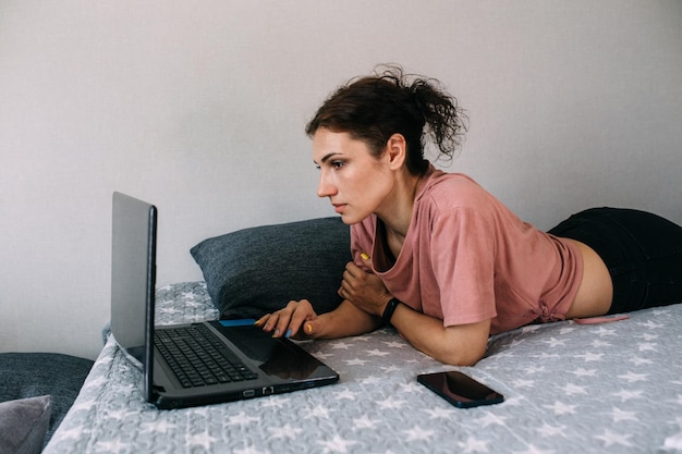 Frau, die mit Laptop arbeitet und auf der Couch liegt Freiberuflich tätig und von zu Hause aus arbeiten