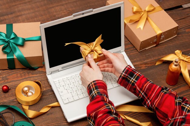 Frau, die mit Laptop-Computer arbeitet und Geschenkboxen auf einem Tisch einwickelt.