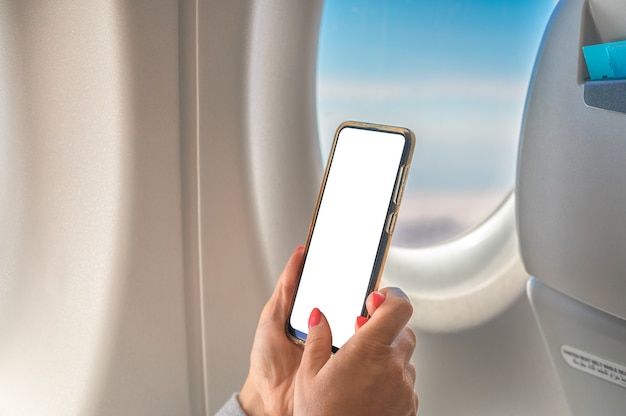 Frau, die Modell-Handy beim Sitzen im Flugzeug benutzt Frau, die Smartphone im Flugzeugflug verwendet.