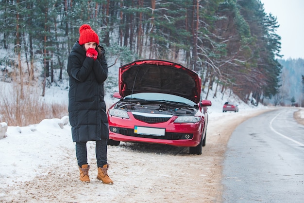 Frau, die Motor defektes Auto im Winterstraßenseitenkopierraum betrachtet