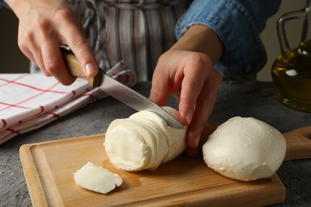 Frau, die Mozzarella auf Holzbrett auf grauem Tisch schneidet, nah oben