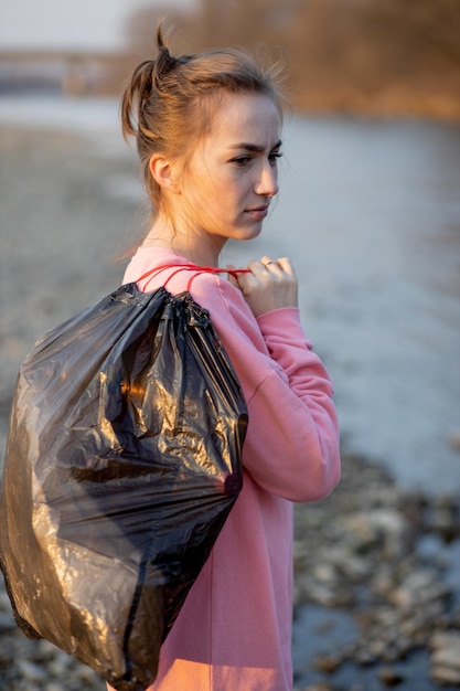 Frau, die Müll und Plastik aufsammelt und den Strand mit einem Müllsack reinigt Freiwilliger Umweltaktivist gegen den Klimawandel und die Verschmutzung der Flüsse