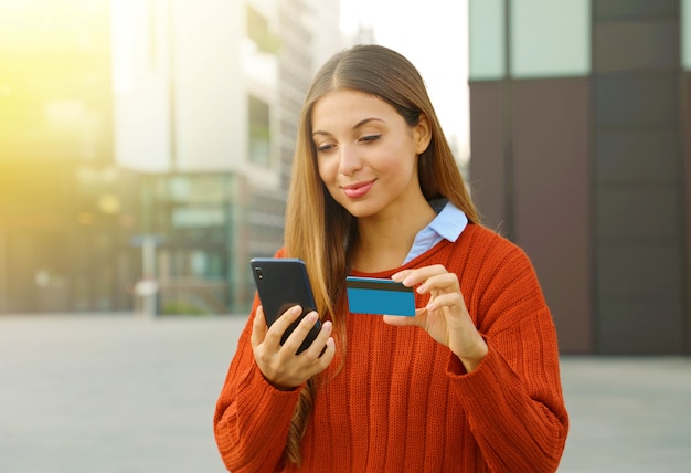 Frau, die online mit Smartphone und Kreditkarte im Freien zahlt