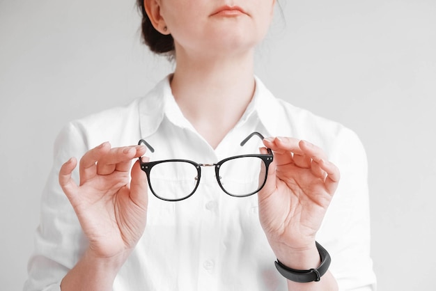 Frau, die optische Gläser in einem schwarzen Rahmen auf einem weißen Hintergrund hält. Kopieren, leerer Raum