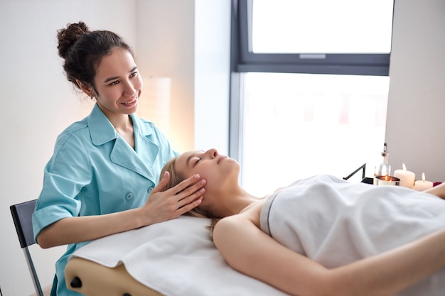 Frau, die osteopathische oder chiropraktische Behandlung im Gesicht und am Kopf in Klinikseitenansicht auf weibliche...