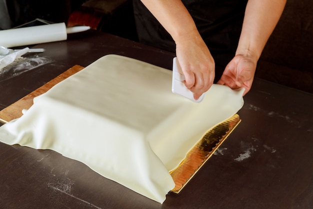 Frau, die quadratischen Kuchen mit weißem Fondant verziert, der Hochzeitstorte macht