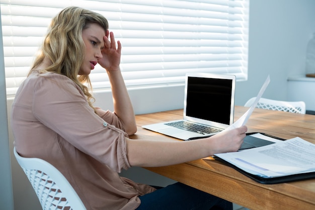 Frau, die Rechnung beim Verwenden des Laptops betrachtet