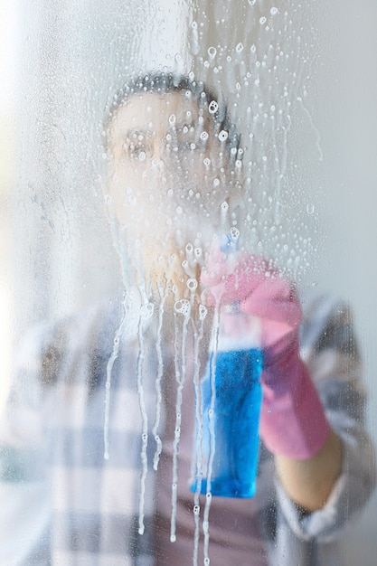 Frau, die Reinigungsspray verwendet, um das Glasfenster zu Hause zu reinigen